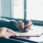 Woman in sweater planning integrated marketing checklist at desk